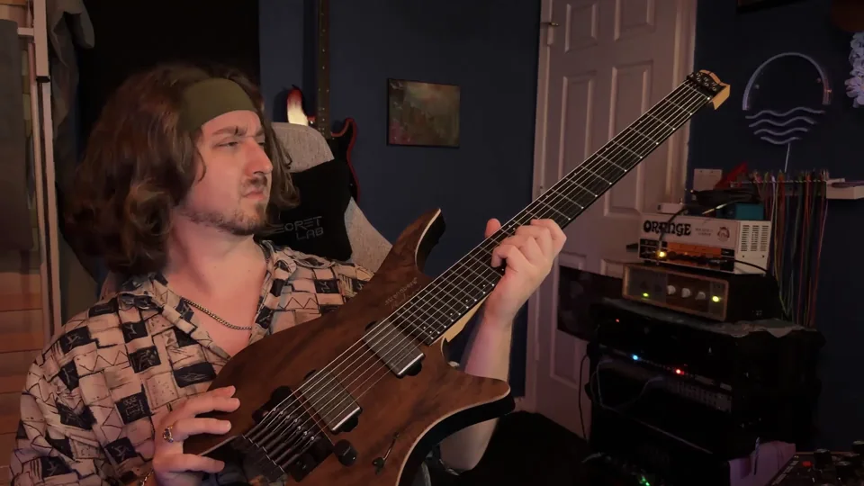 Jacob holding an extended-range guitar in the studio, looking toward the camera
